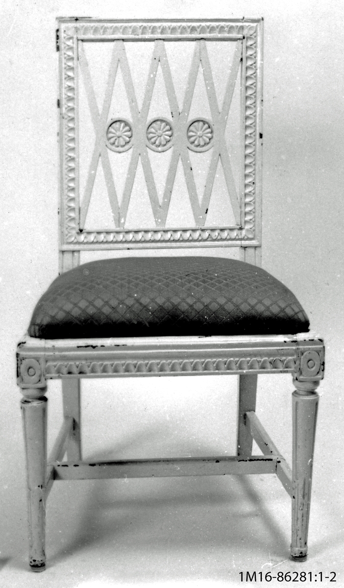 Vitmålad gustaviansk stol tillverkad i Lindome, svarvade framben, sk nagelkärning i rygg och sargar, diagonala spjälor i rygg med 3 st svarvade och skurna brickor. Stoppad och klädd sits, tvärslåar.