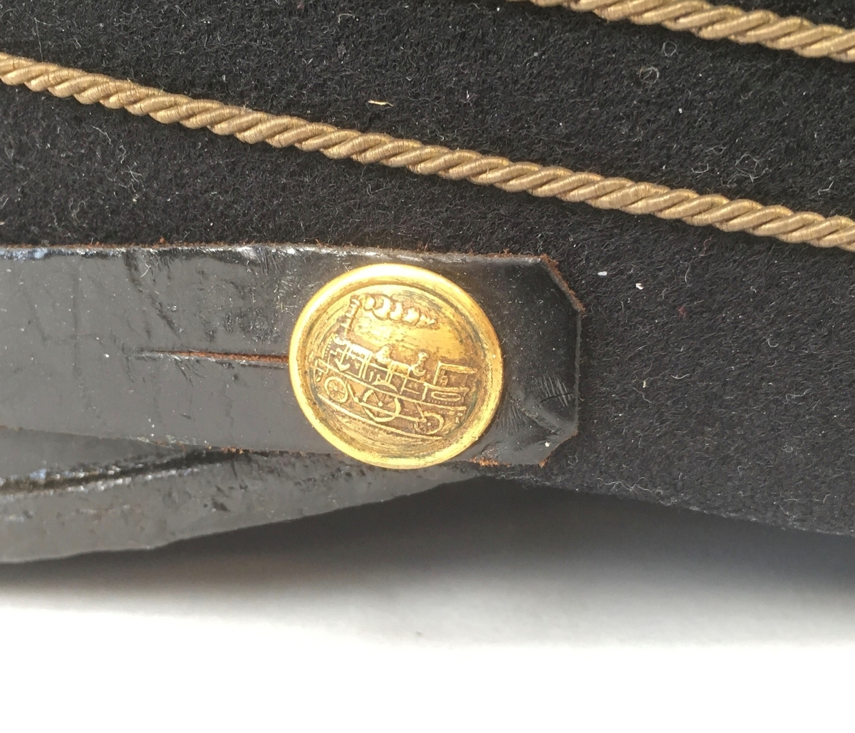 Uniformsmössa av 1899 års modell, av fint svart kläde med kort lackskärm. Mössan har tre guldfärgade galoner, samt blåemaljerad mössknapp med guldfärgat A-lok och guldfärgat vinghjul av 1921 års uniformsreglemente för Enskild järnväg (EJ). Förutom vinghjulet är alla delar av 1899 års modell. Mössbandet är av läder, fastsatt med guldfärgade mösstränsknappar med A-lok.
Mössan är fodrad med svart bomullssatäng. Inuti sitter en fastsytt vävt etikett från Rörströms & Co, Stockholm.