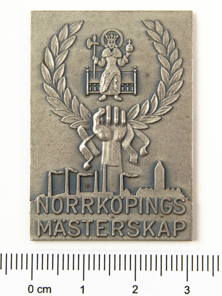 Plakett, Norrköpings mästerskap, silver. På framsidan en relief med en knuten hand och lagerkrans under Norrköpings kommunvapen. Under handen en kuliss med fabriker och texten "Norrköpings mästerskap".
