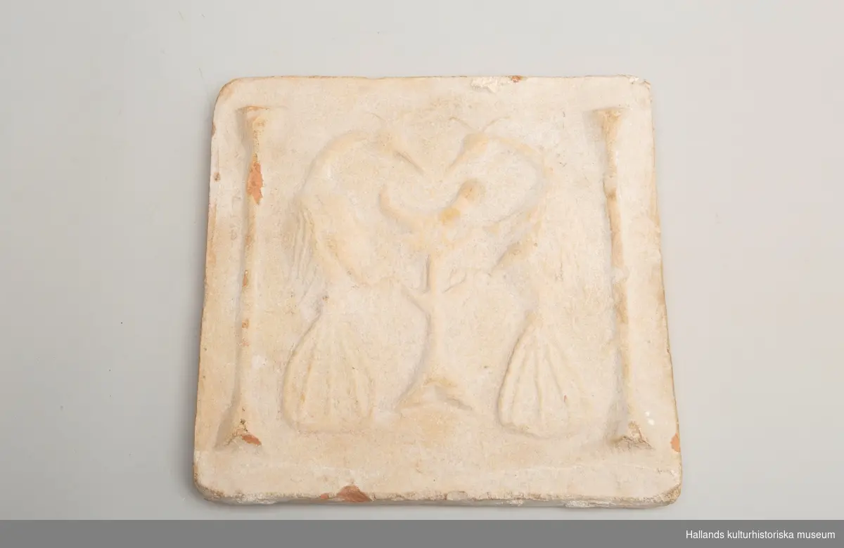 Keramikplatta med motiv av två fåglar med träd i mitten och sidodekorationer. fyrkantig. Små bitar fallit bort. 