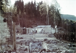 Soldater marsjerer forbi ruinen av et hus i en skog.