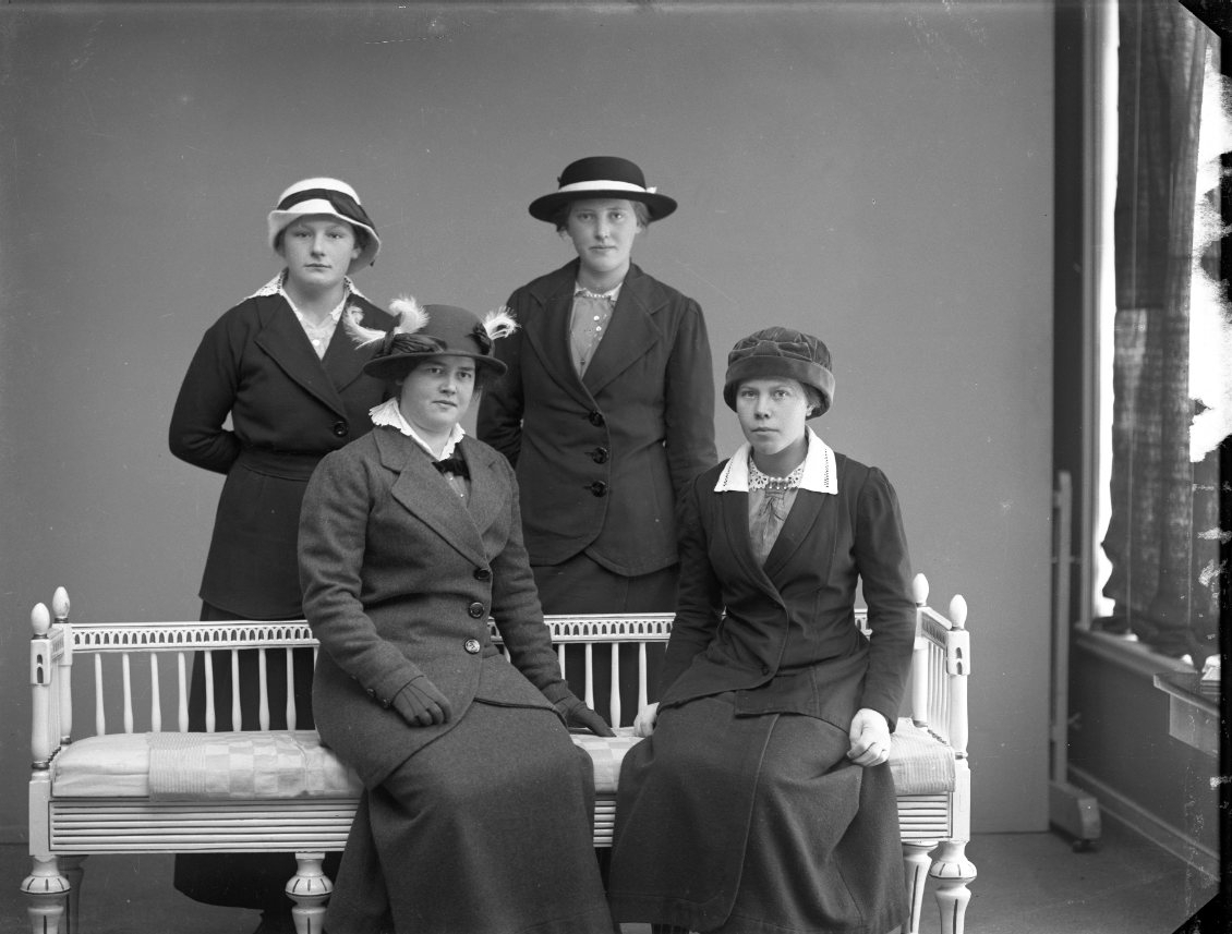 Fyra unga kvinnor med hatt på huvudet. Två av dem sitter i en soffa av gustaviansk stil. Någon av kvinnorna är Gertrud Björkman från Gränna.