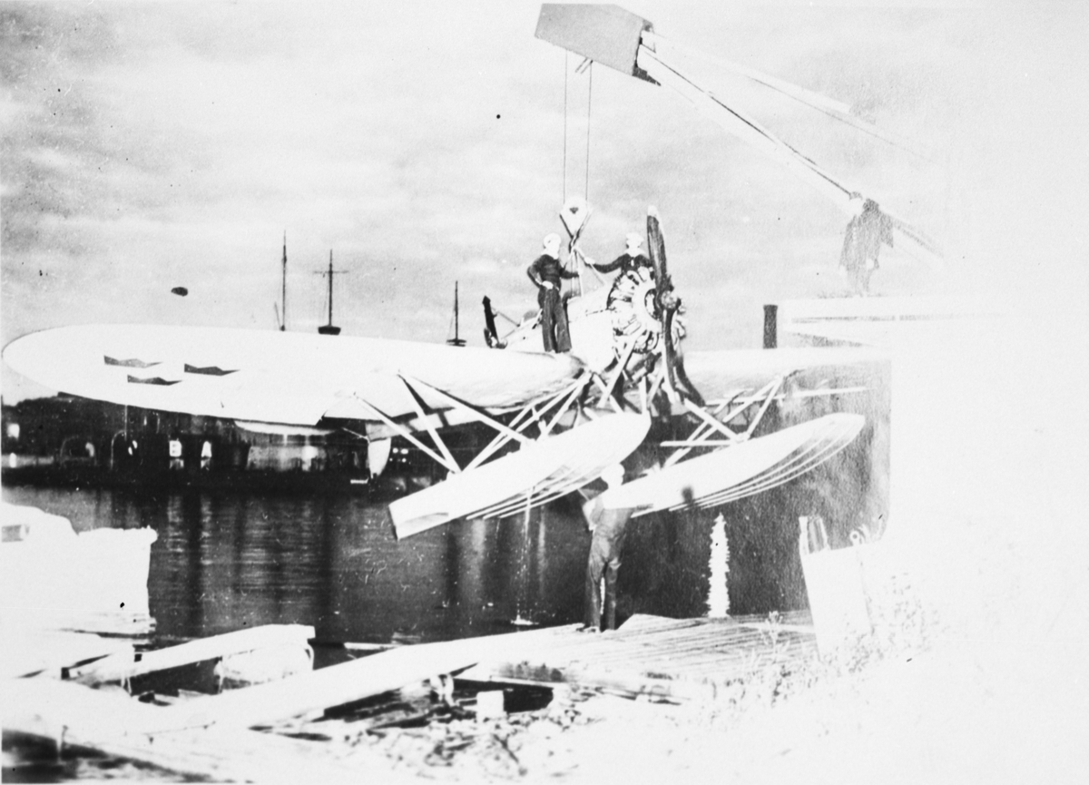 Flygplan S 5 Heinkel He lyfts upp med kran ur vattnet vid en hamn. Två marinsoldater står på flygplanets vingar.