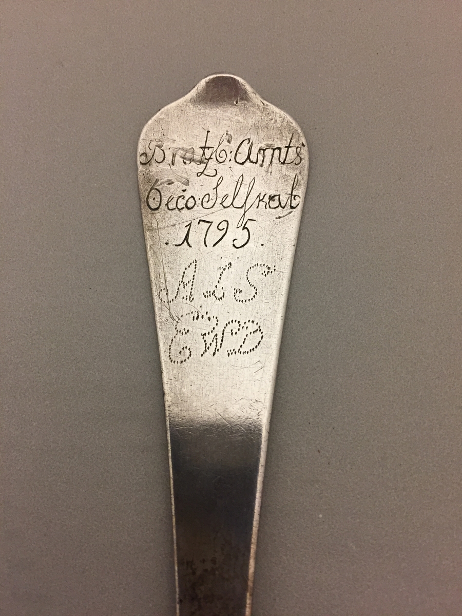 Gamal sølvskei i to delar. Inskripsjonar på skaftet. Årstalet 1795 og bokstavane ALS EWD Gravera rosemønster på baksida av bladet.