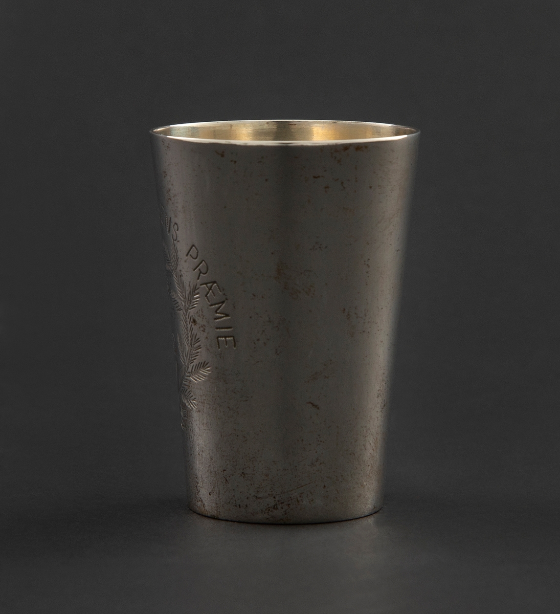 Pokal i sølv formet som et beger med svakt konisk korpus. Korpus er gravert med krans, sløyfe og stjerne sammen med innskrift.