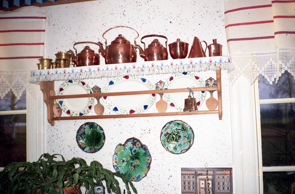 Interiör från köket i Sunnanåker, 8 november 1999. På väggen sitter en hylla där det står tallrikar, slevar, föremål av koppar och mässing.
