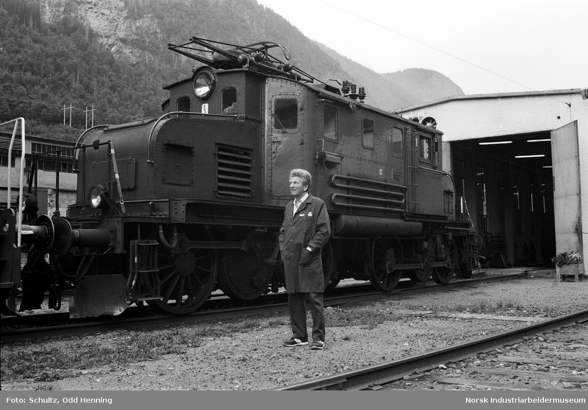 Mann utenfor Rjukanbanens elektriske lokomotiv nummer 14. Lokomotivet står på jernbanespor utenfor lokomotivstallen.