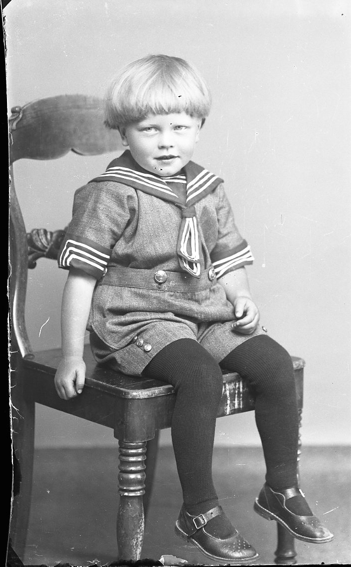 Porträtt av en liten pojke i sjömansdräkt som sitter på en stol.