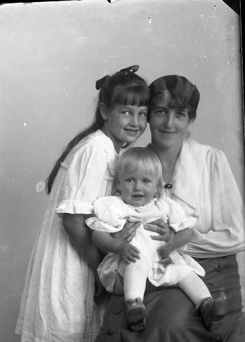 En kvinna sitter på en stol med två barn tätt intill sig, varav en flicka står intill och ett spädbarn i kvinnans knä. Kvinnan är fru Hård af Segerstad i Växjö.