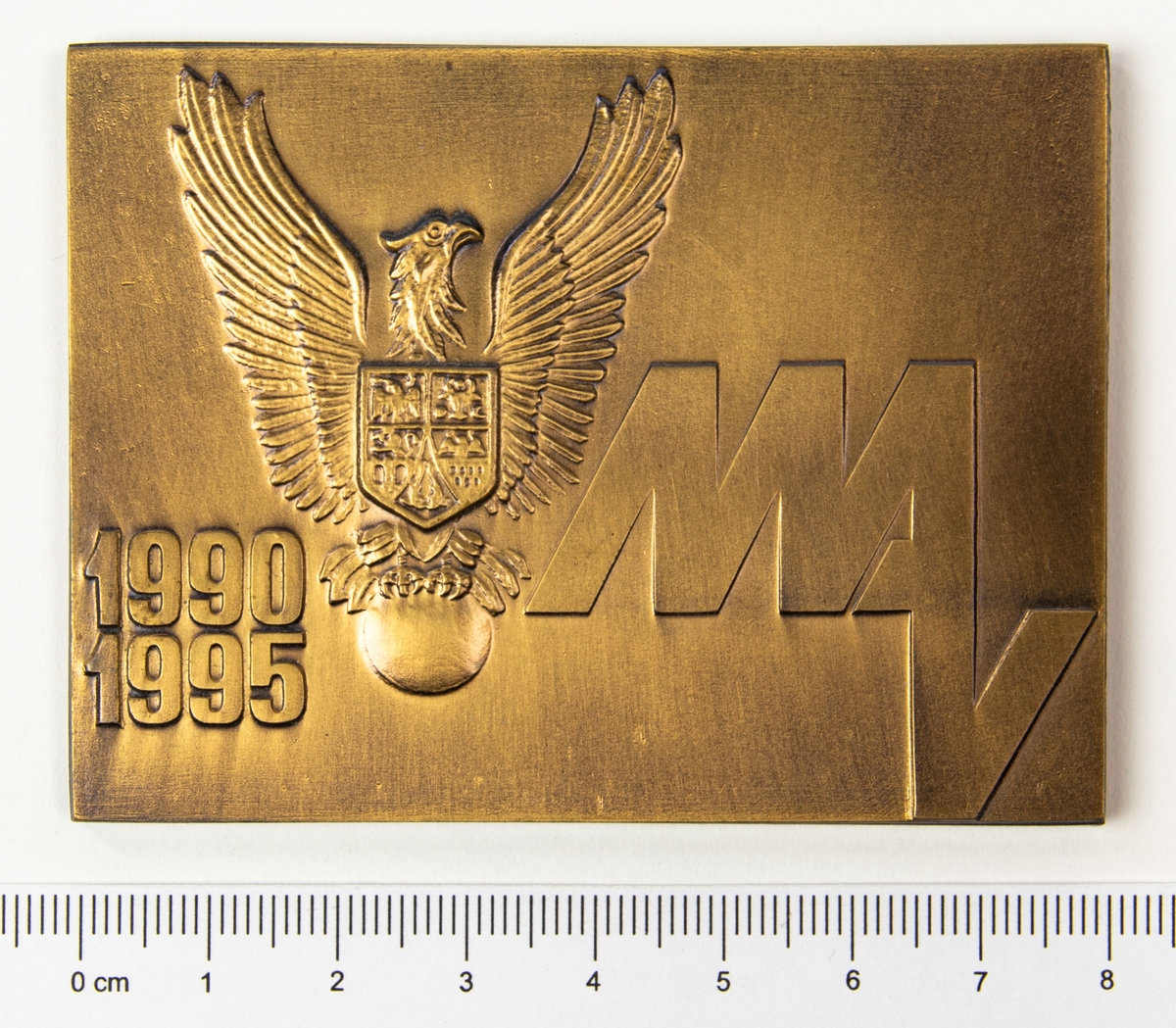 Minnesplakett med motiv av en örn med en sköld på bröstet och texten MAV, årtalen 1990 och 1995 på framsidan. På frånsidan texten Muzeul Aviatiei. Plaketten förvaras i en brun ask.