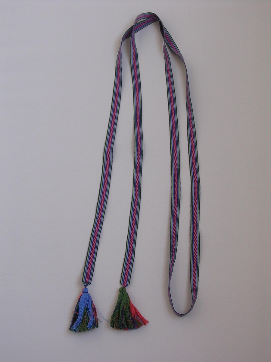 Handvävt bomullsband, rips, i rosa, grönt och två blå nyanser.
Tofsar i båda ändar, 9 cm långa.

Funktion: Bara, Stor högtidsdräkt, Skåne