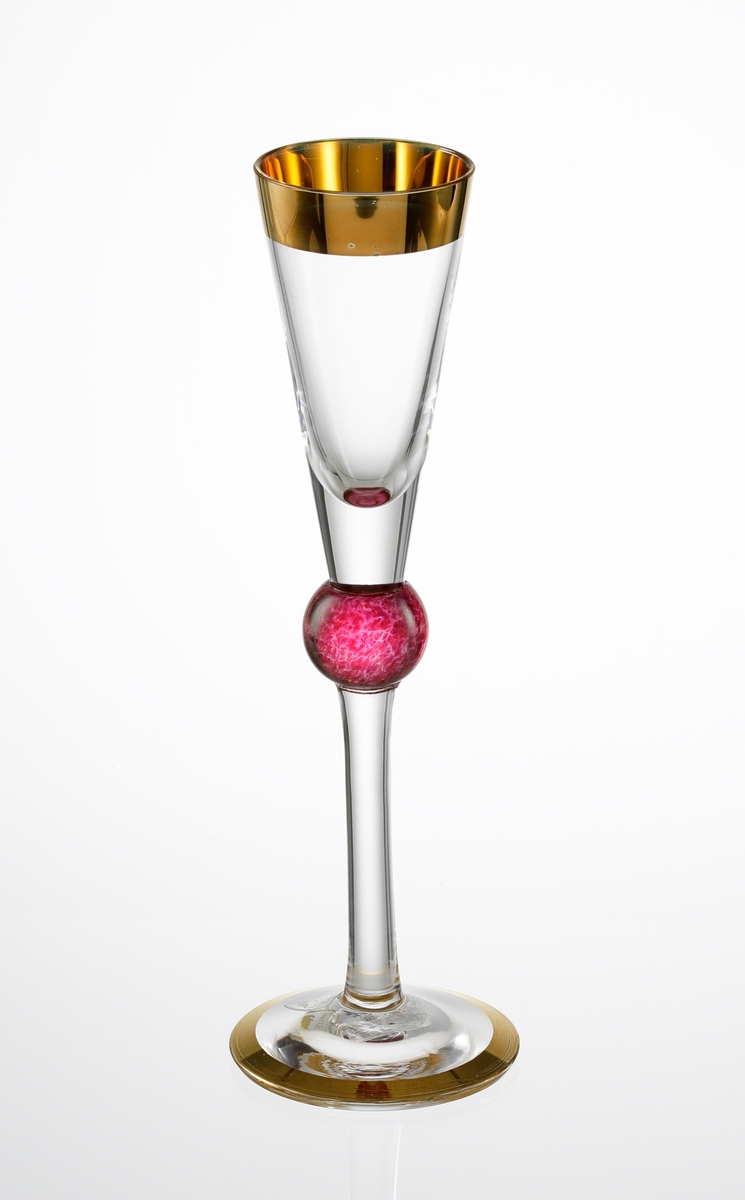 "Millenium" Formgivare: Erika Lagerbielke. Konisk kupa med guld runt mynningskant. Kula i rosa-röttt. Fot med guldmålad kant. 
Snapsglaset togs fram som komplement till champagneglasen, som formgavs till millenieskiftet 1999/2000 (se OF1635-1-3), tillsammans med vinglas, ölglas, avec, och tumblers.
Snapsglasen var tänkta att fungera i par, där det ena glaset skulle vara något högre än det andra, samt att de skulle skilja sig åt i fråga om färgen på kulan. Detta är det något lägre glaset.
Ofärgad etikett med orre och text i silver.