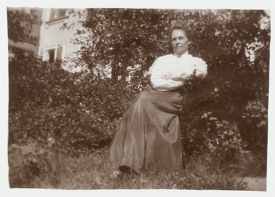 En okänd medelålders kvinna i blus och kjol har slagit sig ner i en trädgård, ca 1910.