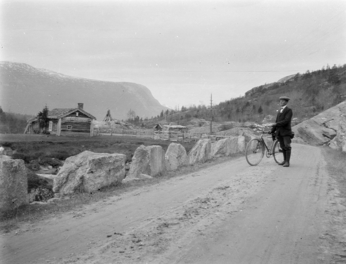 Anton Skotte med sykkel langs gamlevegen ved Rolvstugu, Lesja, som lå under Bakken. Stabbesteiner langs vegen. I bakgrunnen Brøstkampen, Svabotnen og Borge, og Toppen synes så vidt til høyre bak åsen