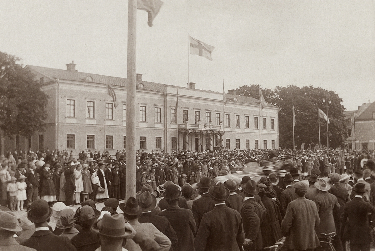 Gustaf V på besök i Växjö, 1920-tal. Man har just lämnat landshövdingens residens vid Stortorget med bil.
Mycket folk har samlats.