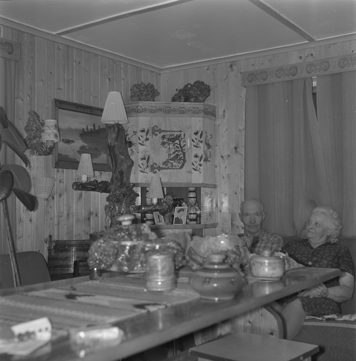 Ola og Maria Odland heime i stova på Meland i Etne, 1977. Til venstre i bileta er døme på trearbeidet til Ola.