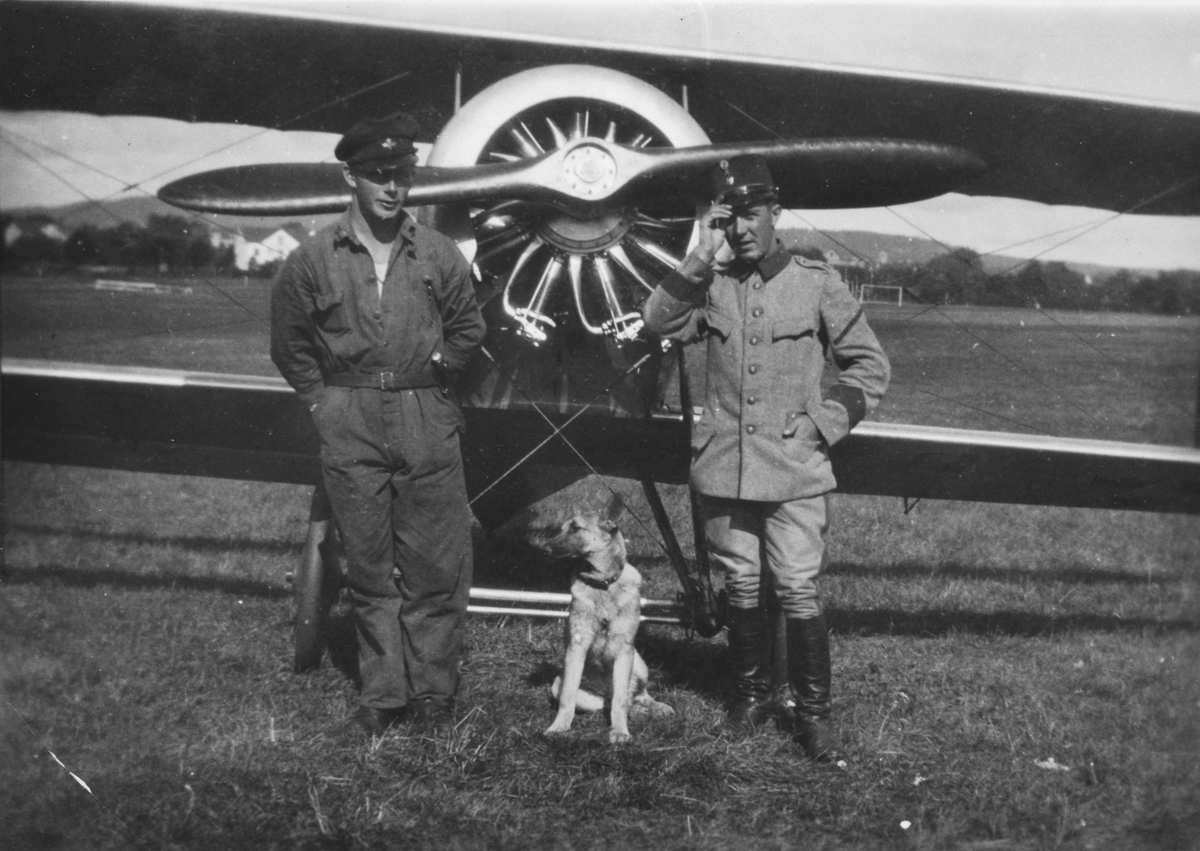 Porträttfoto av två flygsoldater och en hund framför flygplan Tummeliten.