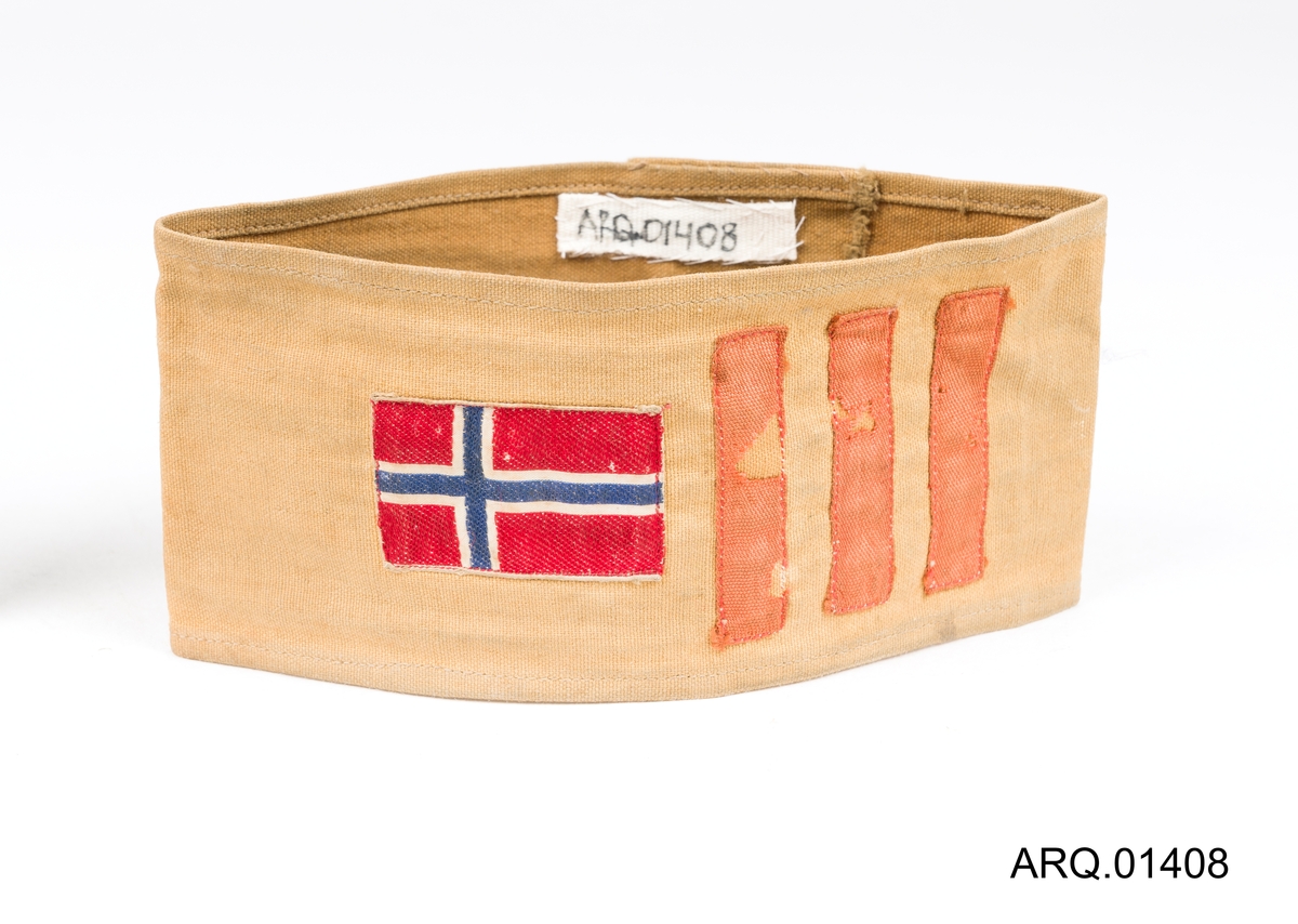 Armbind i seildukstoff, lysegult med påsydd norsk flagg og 3 røde striper.