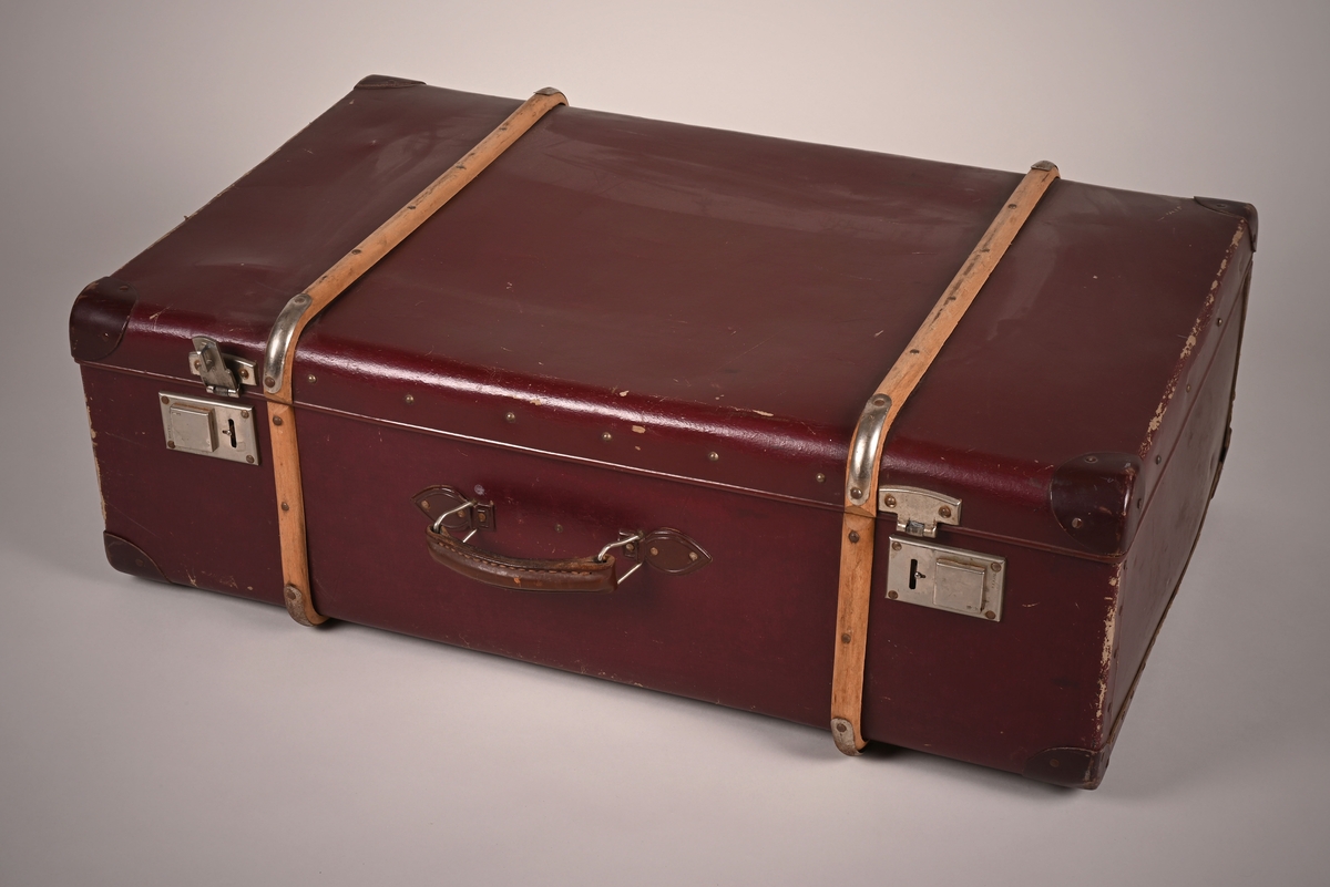 Koffert i rødbrunt skinn med låser av metall. To trebeslag er festet rundt koffertens kropp, og hjørnene er sikret med metallbeslag.