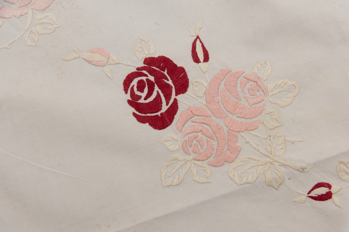 Duk, brodert kaffeduk i bomull med roser i fargene rød og rosa med blader i hvitt plattsøm, heklet blonder 5 cm brede påsydd i kantene