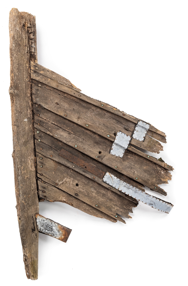 Babords förstäv från en träbåt. På sidan finns plåtar i metall som använts som lagningar över runda hål, varav vissa tros vara från beskjutning.