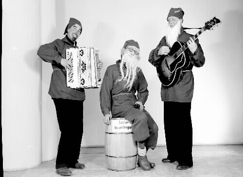 Tre musicerande tomtar; en med dragspel och en har gitarr. En tunna framför dem är märkt med "Luciainsamlingen". Beställare: Tage Sandberg.