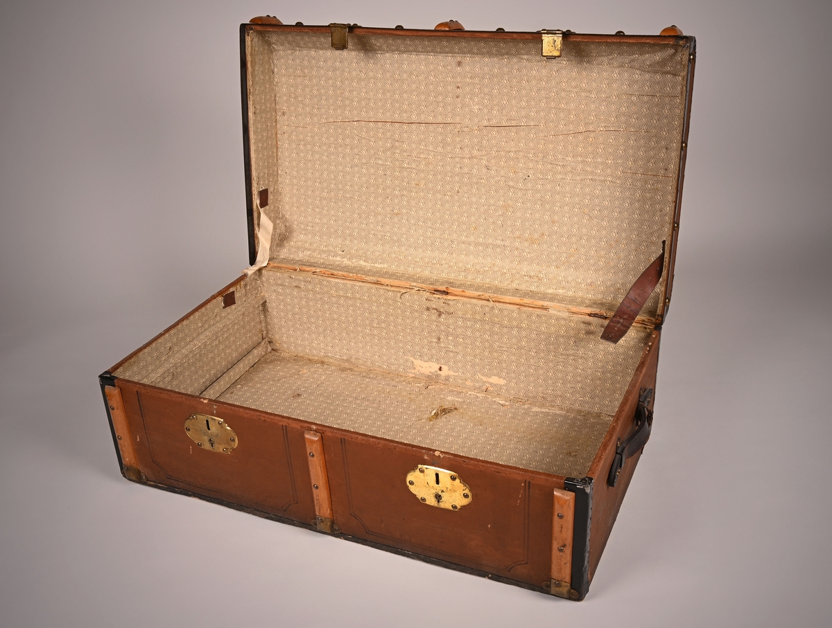 Koffert laget av tre, papp og skinn. Innsiden er kledd med papir. Den lukkes i front med to beslag. På sidene er det festet bærehåndtak av skinn.