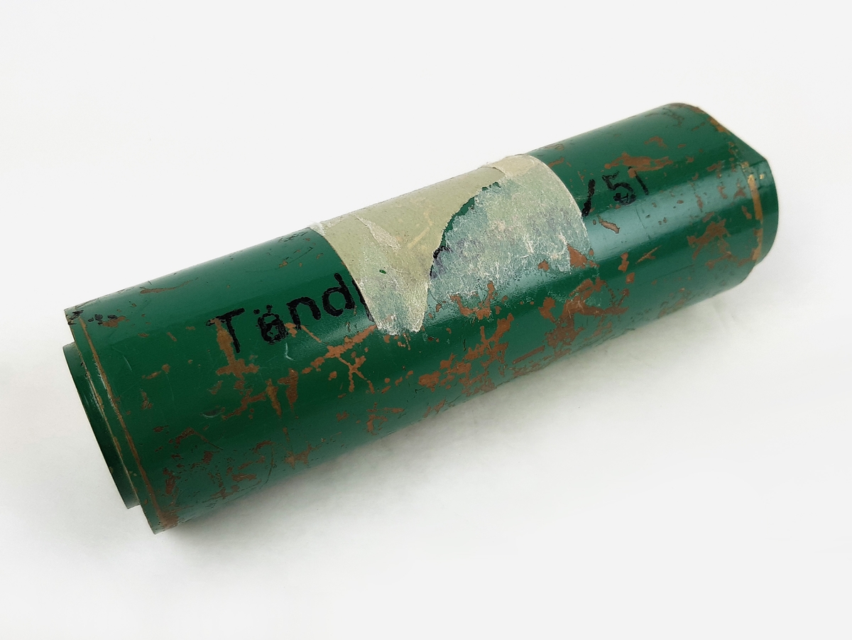 Tändpatron m/51, bestående av en cylinderformad kapsell i grönmålad metall. Vid sidan märkt "Tändpatron m/51". Samt märkt "BLIND" på kortsidorna.
