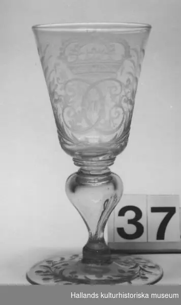 Pokal av glas med Karl XII:s krönta monogram i bladcartouche. Fot med graverad växtranka. Droppformig ihålig midja. Böhmisk typ.