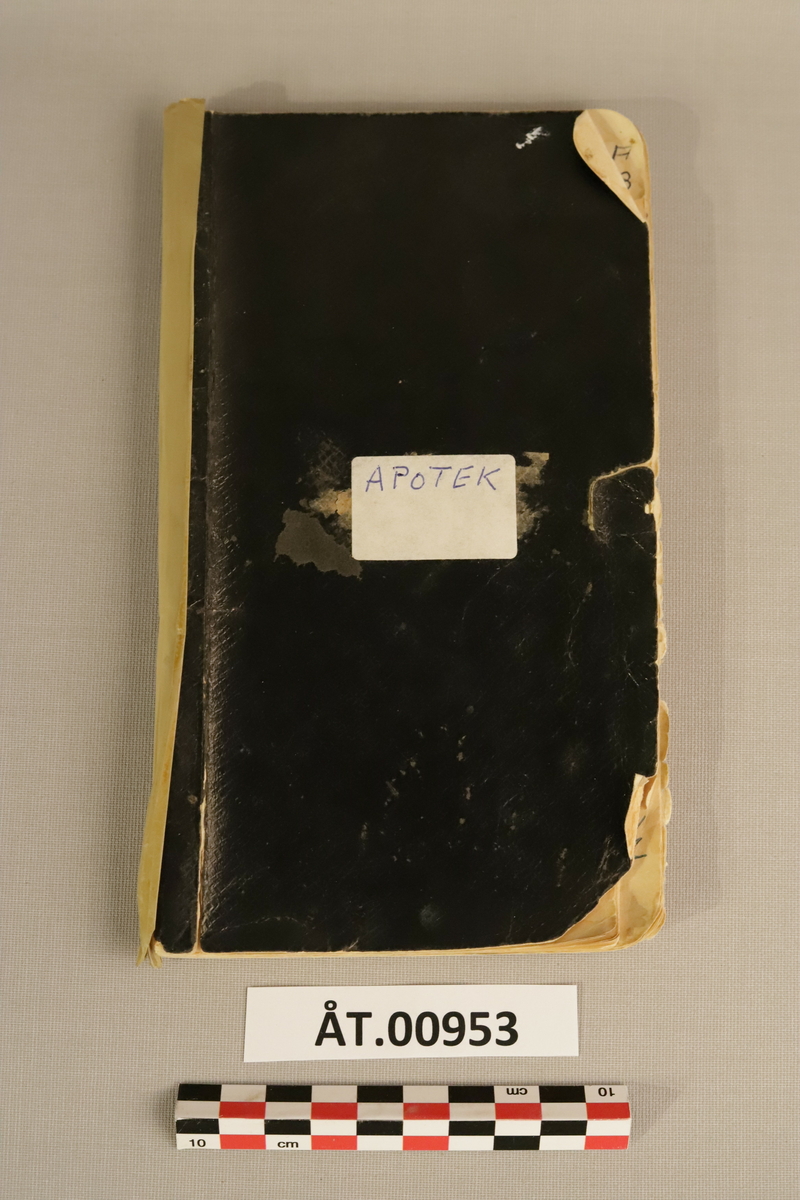 Svart notatbok med kvit påklistra lapp med teksten: Apotek. Tekst elles: Per Birkeland. Med Alfabetisk inndeling 