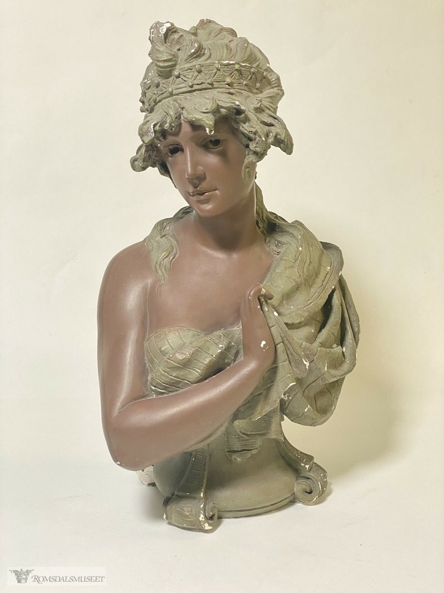 Halvfigur av en kvinne med toga/sjal, hårbånd, som holder en hånd opp mot brystet.