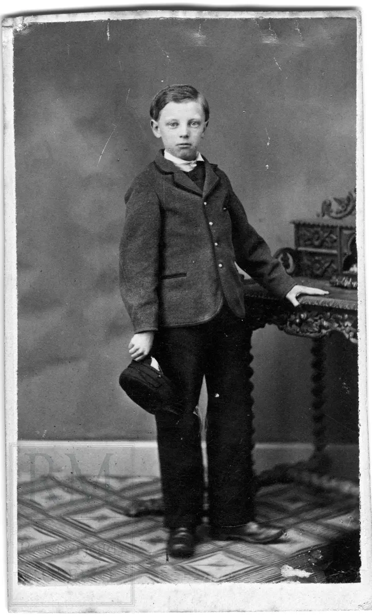 En gutt står med en lue i hånda og holder seg i et skrivebord.