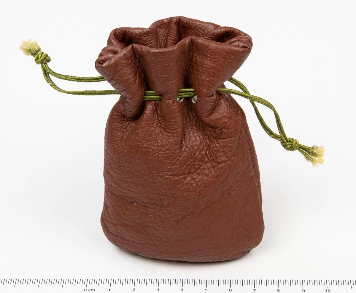 Miniatyrer som förvaras i en rödbrun läderpåse. 
Miniatererna består av en stor blandning av objet; amuletter, souvenirer, berlocker, en tärning med flera.