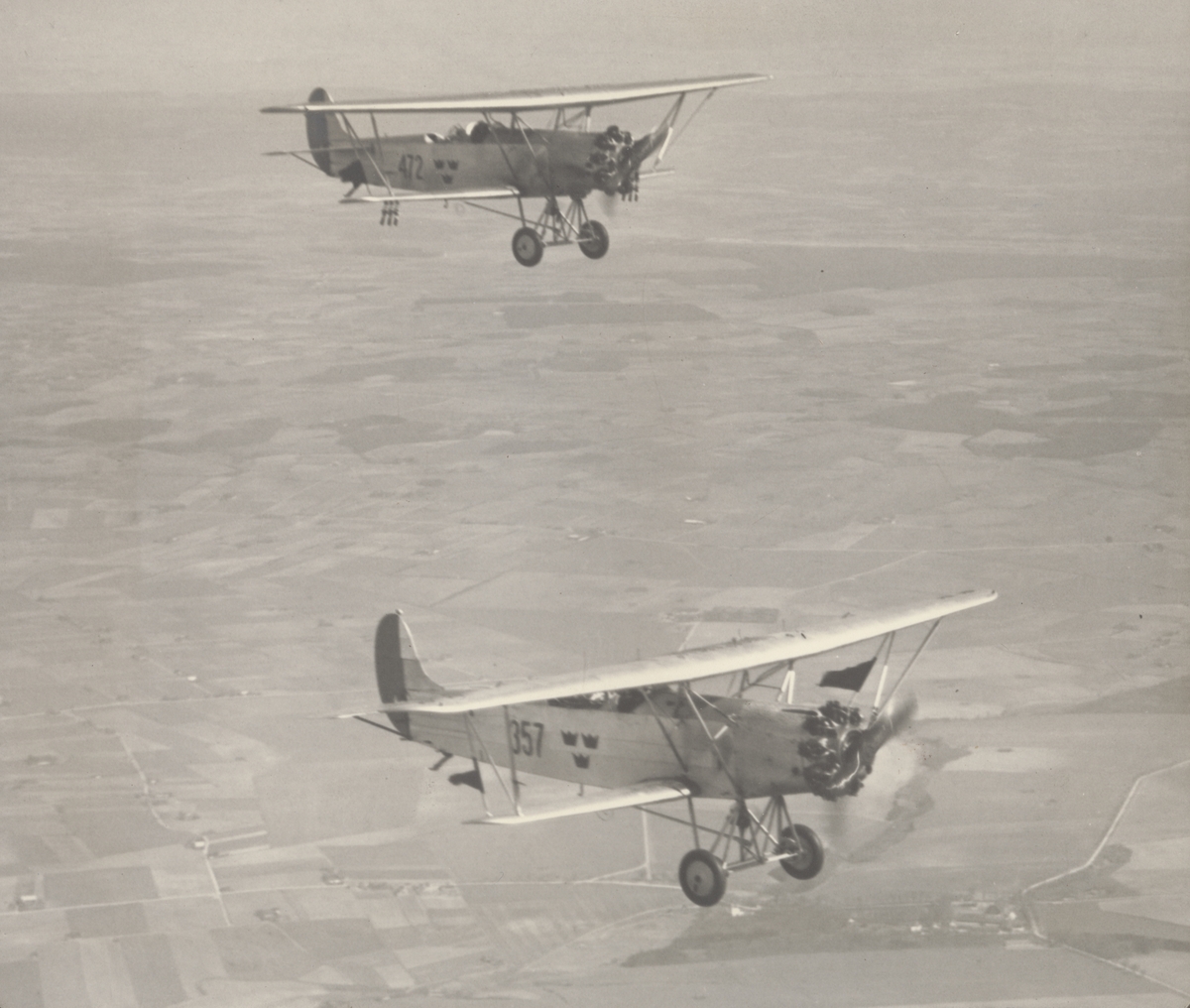 Flygbild av två flygplan S 6, Fokker C.VE i luften över landskap, 1930. Flygplan nr 357 och 472.