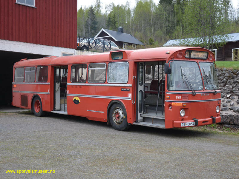 Buss med rødt eksteriør og to doble dører. Rundt bussen går en hvit og sort stripe. Bussens interiør består av lyst grått gulv og lyse tak med vinrøde seter. 