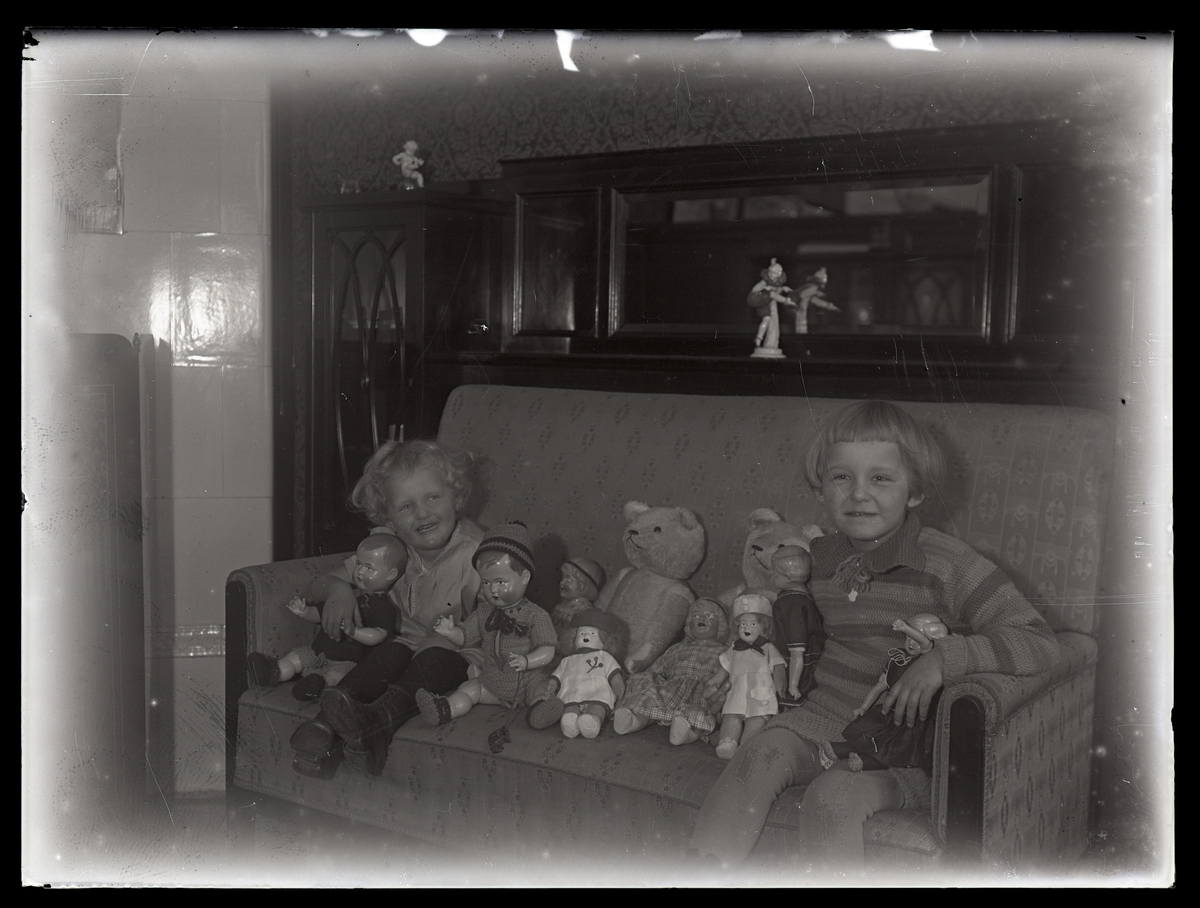 Två småflickor sitter i soffa med sina dockor och nallar. Västerås.