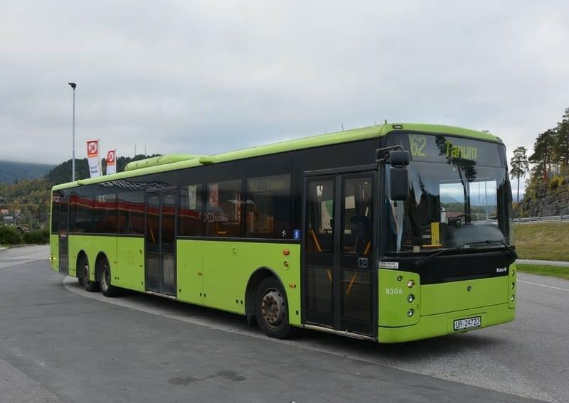 Grønn og svart buss med tre dobbeltdører. Interiøret består av grå overflater og blå seter. 
