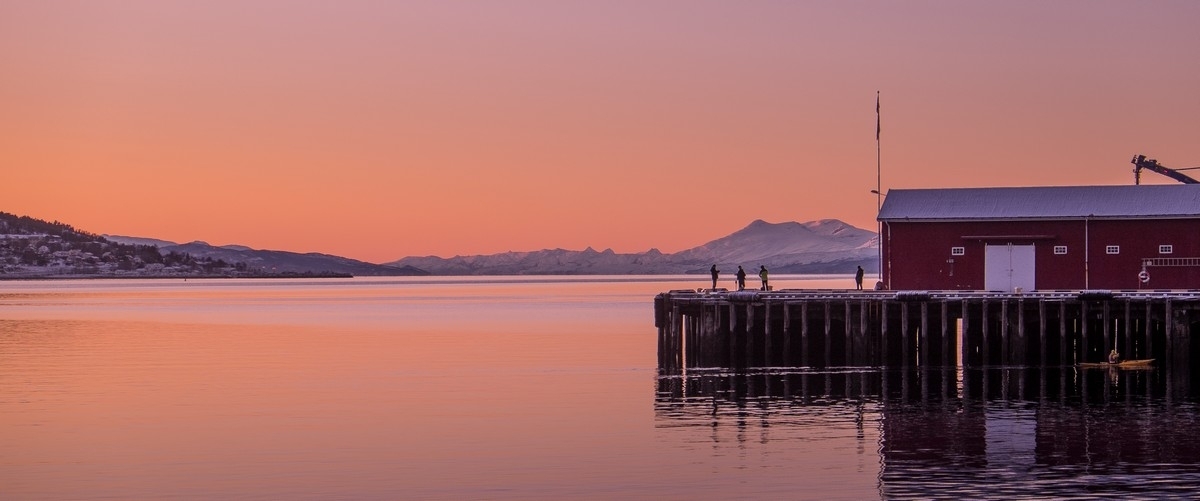Sola under horisonten på Narvik havn 5. februar kl 16:20. Ytterst på piren noen som fisker, og i nedre høyre kant en kajak.