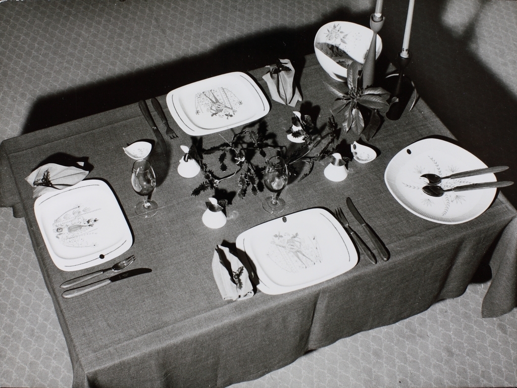 Bord dekket med tallerken fra Stavangerflint AS. Tallerken dekorert med designer av Inger Waage: mann med mandolin og dame med vannkanne