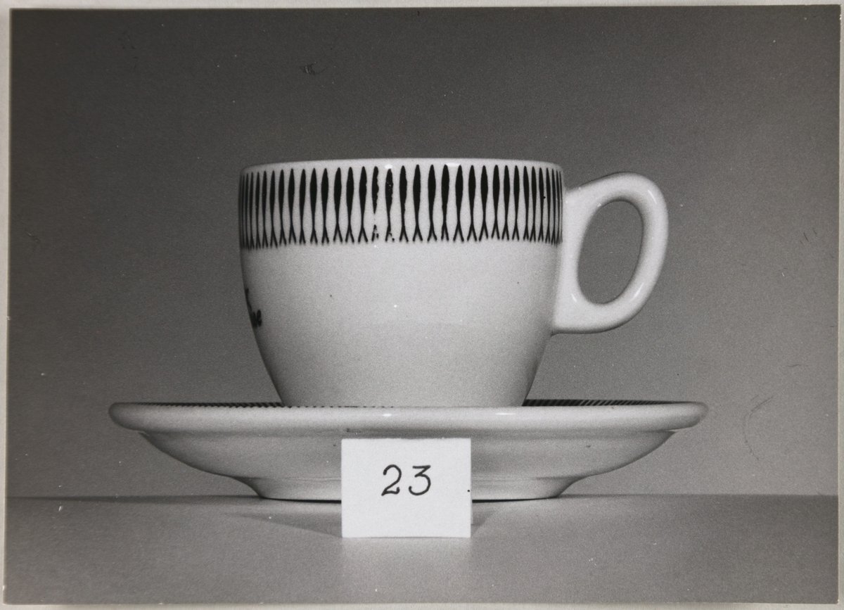 En kaffekopp med underskål fra Stavangerflint AS. I forgrunnen står en lapp med nummeret 23.