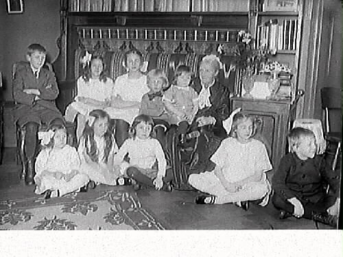 En äldre kvinna sitter omgiven av tio barn i en beramad soffa. Bild 2) Närbild på den äldre kvinnan och barnet i hennes knä.