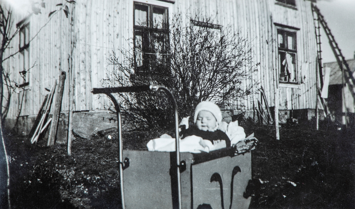 Willy Erland Løvås (f: 23.05.1940) sittende i en barnevogn utenfor huset på bruket Løvås i Stange. Hans far, Erland Andreassen ble drept av tyskerene i kampene ved Strandlykkja den 17. april 1940.