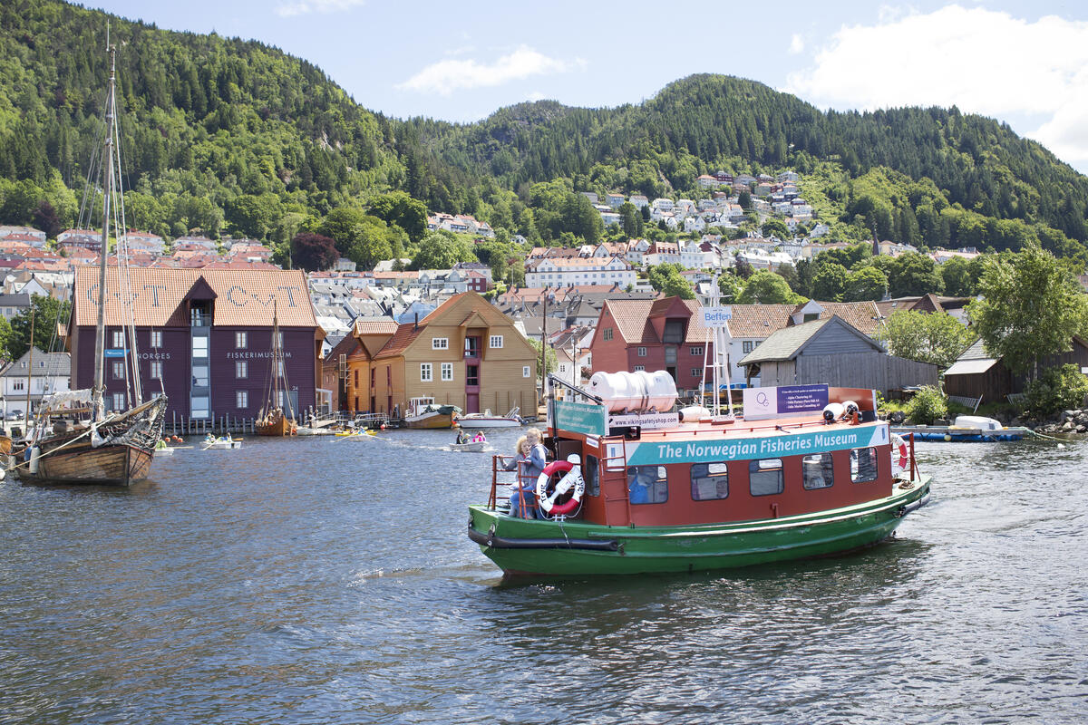 Her ser vi en aktiv havn, med flere robåter og Beffen som kommer inn til Norges Fiskerimuseum