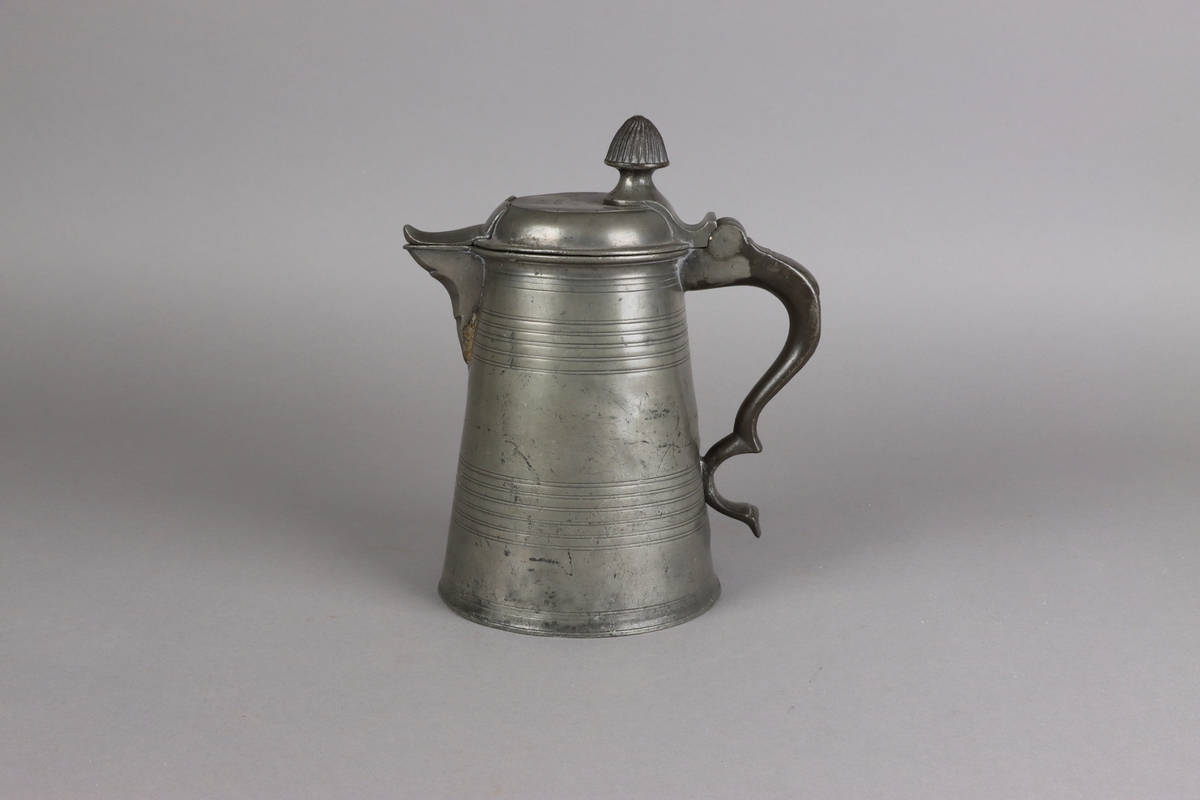Jug and cover, all in pewter, with conical body  and a loop handle. On the cover knob in the form of a pine cone. On the body sections of horizontal borders. Five hallmarks inside the jug.