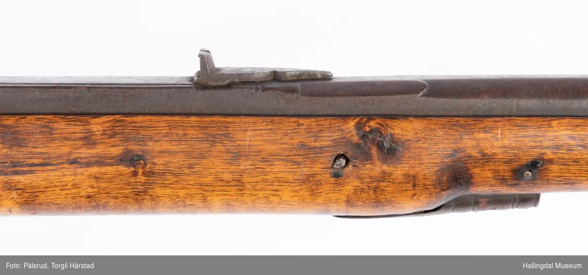 Gevær med perkusjonslås og kassepipe. Kan ha vært ombygd fra flintlås. 
Fra låsen til siktet midt på løpet er løpet kasseformet og har en dekorert overgang til et svakt avrundet åttekantet løp. Det fremste siktet er av messing. Kolbekappen er festet med to skruer. Mangler avtrekksbøyle, reim og ladestokk.