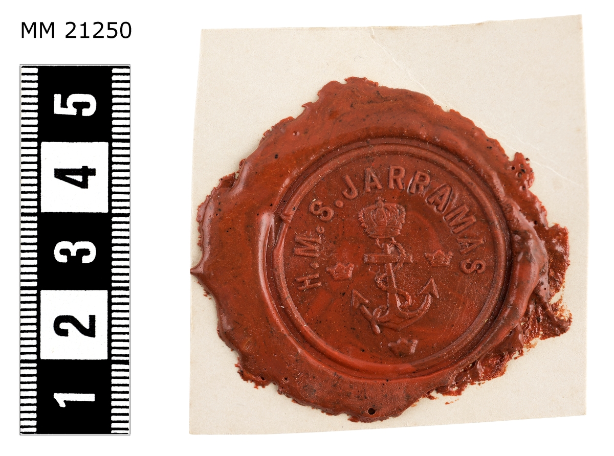 Sigillavtryck av rött lack på papper. I mitten krönt stockankare omgivet av tre kronor. Längs kanten text: "HMS Jarramas".