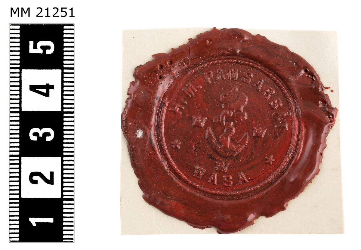 Sigillavtryck av rött lack på papper. I mitten krönt stockankare omgivet av tre kronor. Längs kanten text: "HM pansarbåt Wasa".