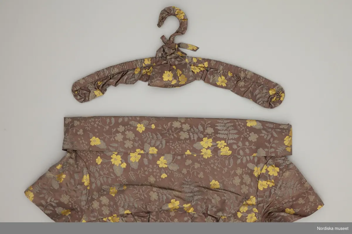 Arrangemang med galgar, specialklädda i samma tyg som plagg uppsydda på NK:s Franska damskrädderi. Inlånade till Nordiska museet i samband med produktion av bok och utställning Nordens Paris. NK:s Franska damskrädderi 1902-1966.