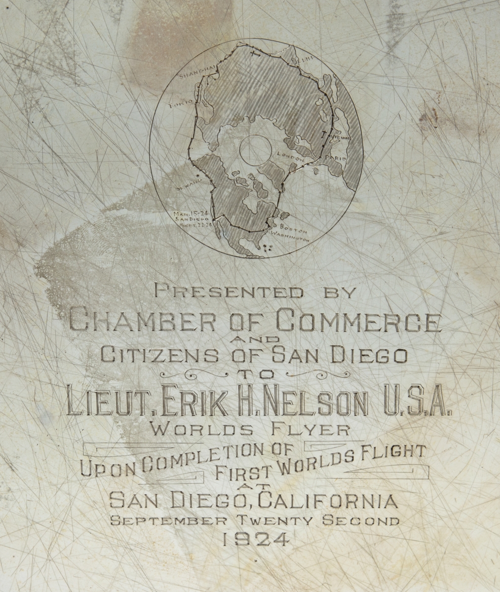 Silverbricka med oval form och utfasade handtag på vardera sida. Text: "Presented by Chamber of Commerce and citizens of San Diego to Lieut. Erik H Nelson U.S.A. Worlds flyer Upon Completion of first worlds flight, San Diego, California September Twenty Second 1924".
