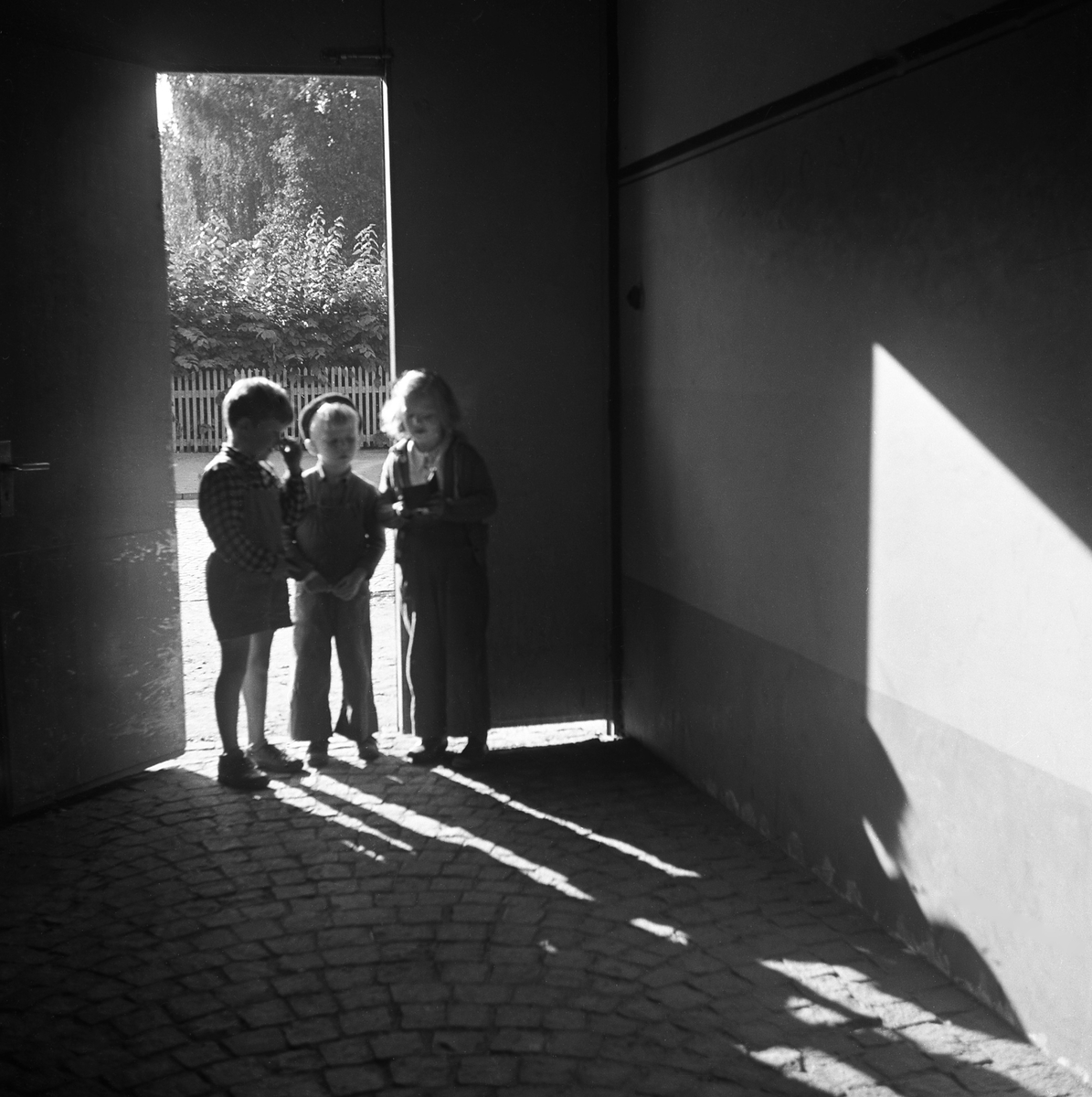 1950-tal. Tre okända barn står i en port.